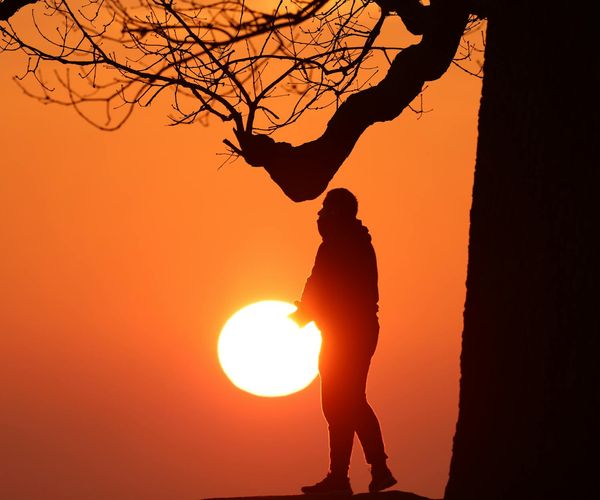 Silhouette of a man stretching against a sunrise, feeling energized.